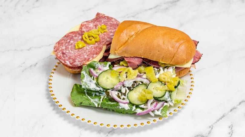 Two halves of a deli sandwich, one with salami and cheese, the other with roast beef and salad.