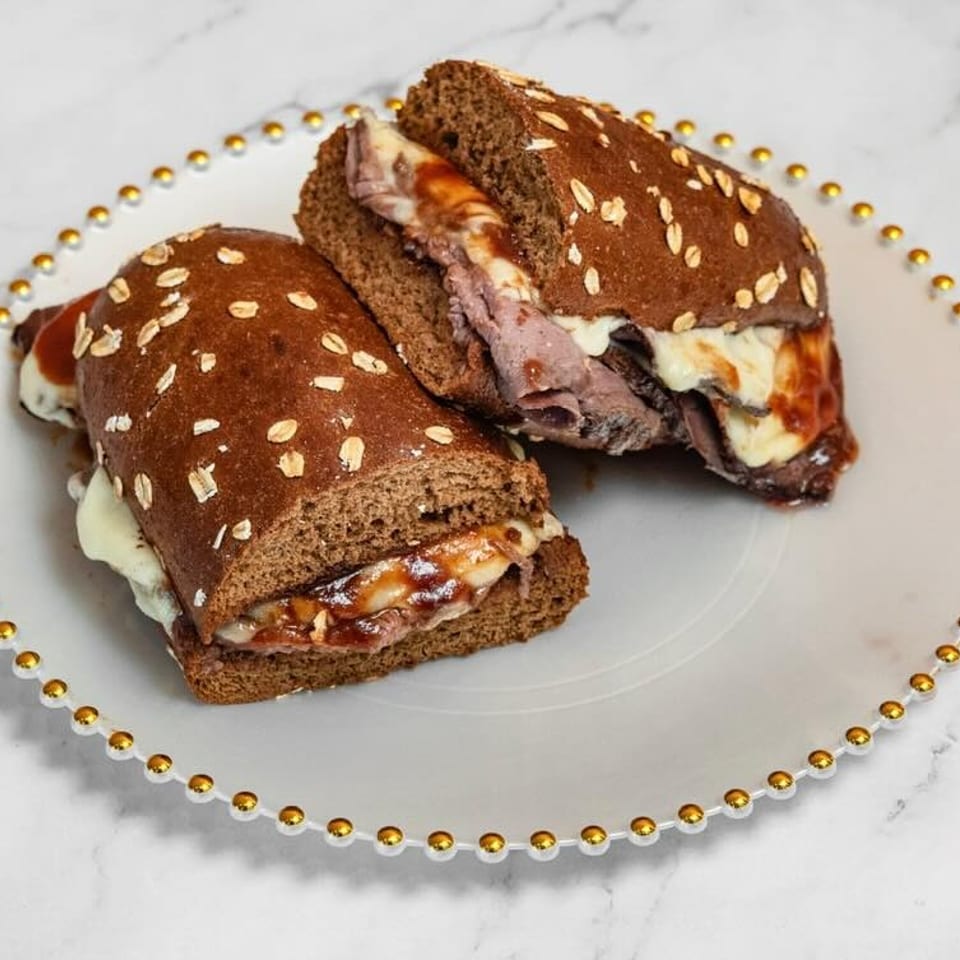 Two halves of a roast beef sandwich with melted cheese and sauce on a white plate.