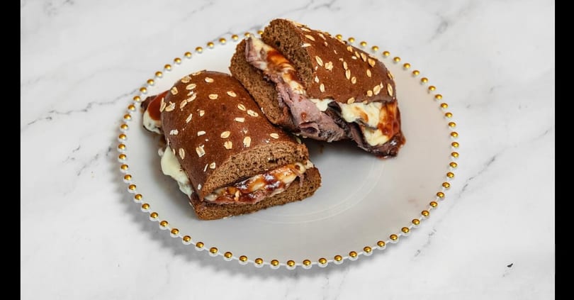 Two halves of a roast beef sandwich with melted cheese and sauce on a white plate.