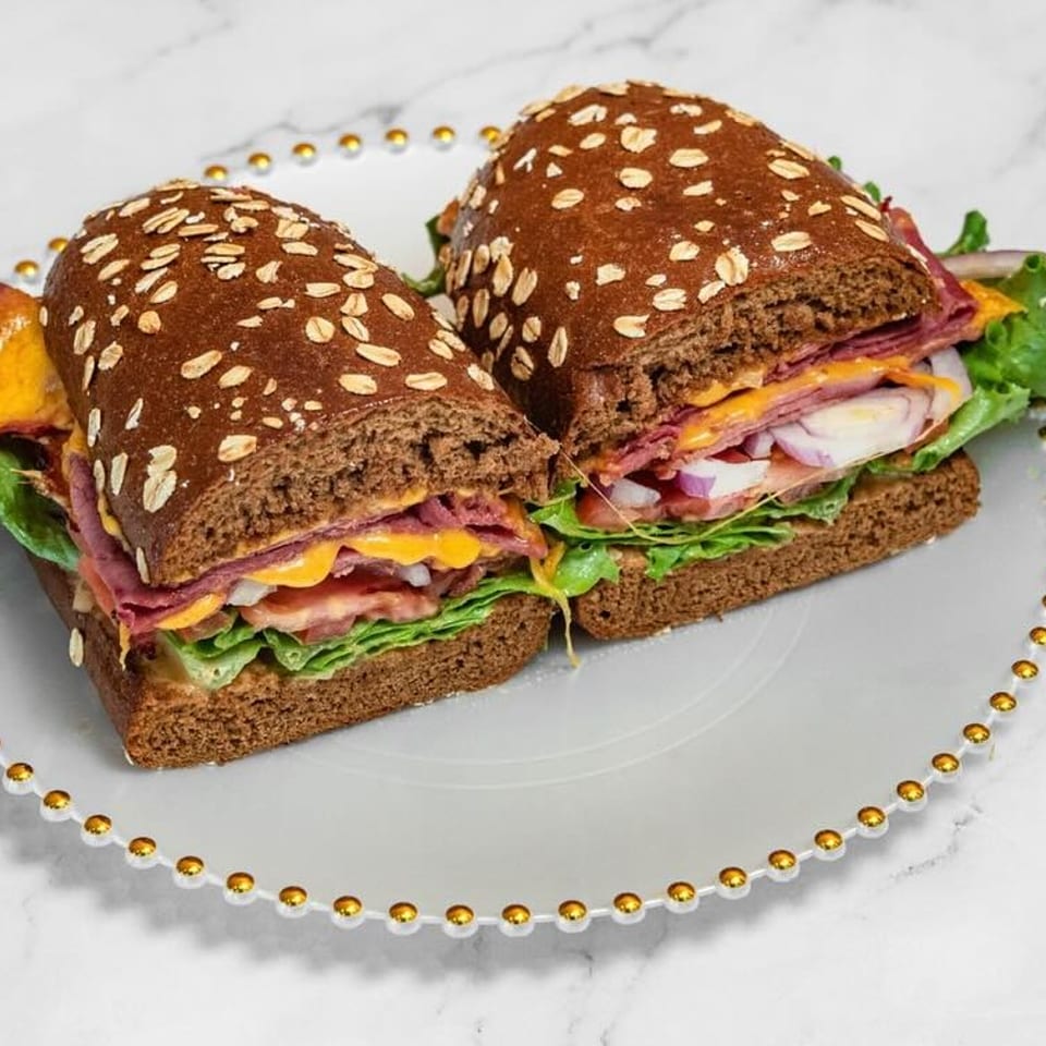 Two halves of a deli sandwich on dark bread with meat, cheese, lettuce, and onions.