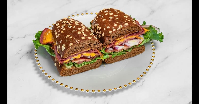 Two halves of a deli sandwich on dark bread with meat, cheese, lettuce, and onions.